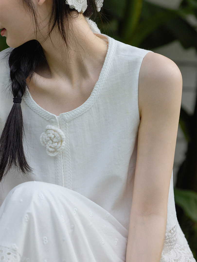 White sleeveless top worn by a model with braided trim and floral detail