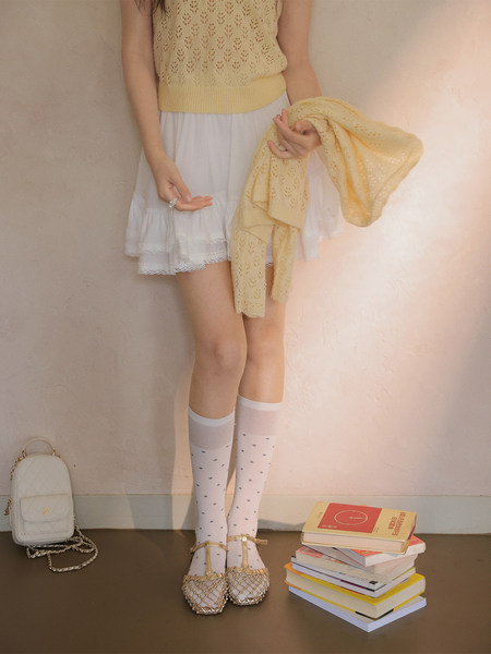Model wearing a pale yellow knit top with a white skirt and gold shoes