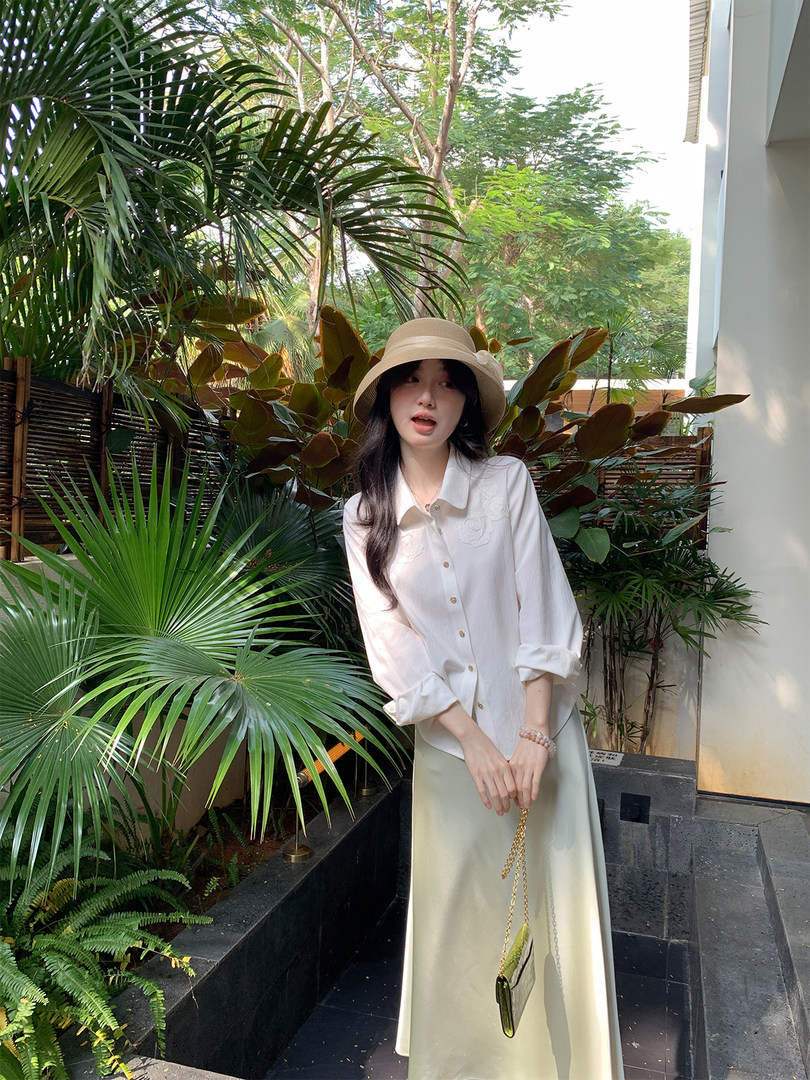 Woman wearing a white button-up blouse, long skirt, and beige hat outdoors