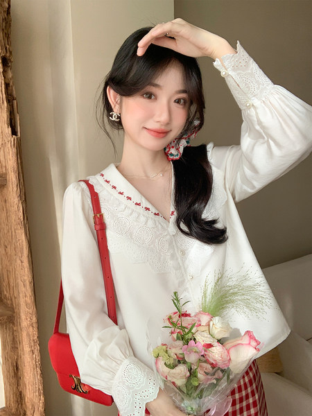 White lace-trimmed long-sleeve blouse worn by a model with a red shoulder bag
