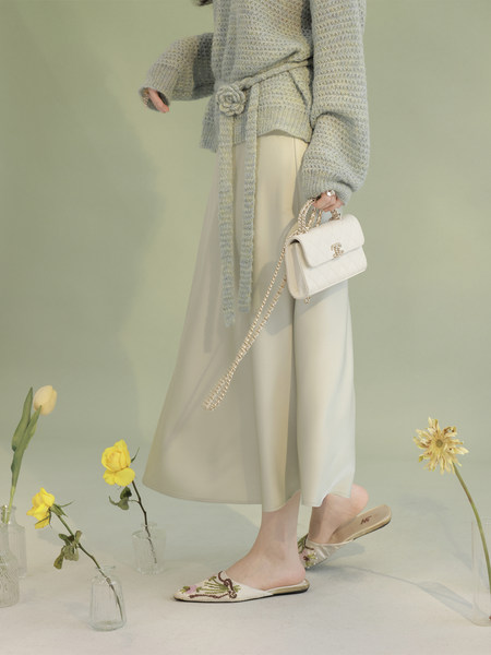 Model wearing a light knit sweater and cream midi skirt holding a white chain handbag