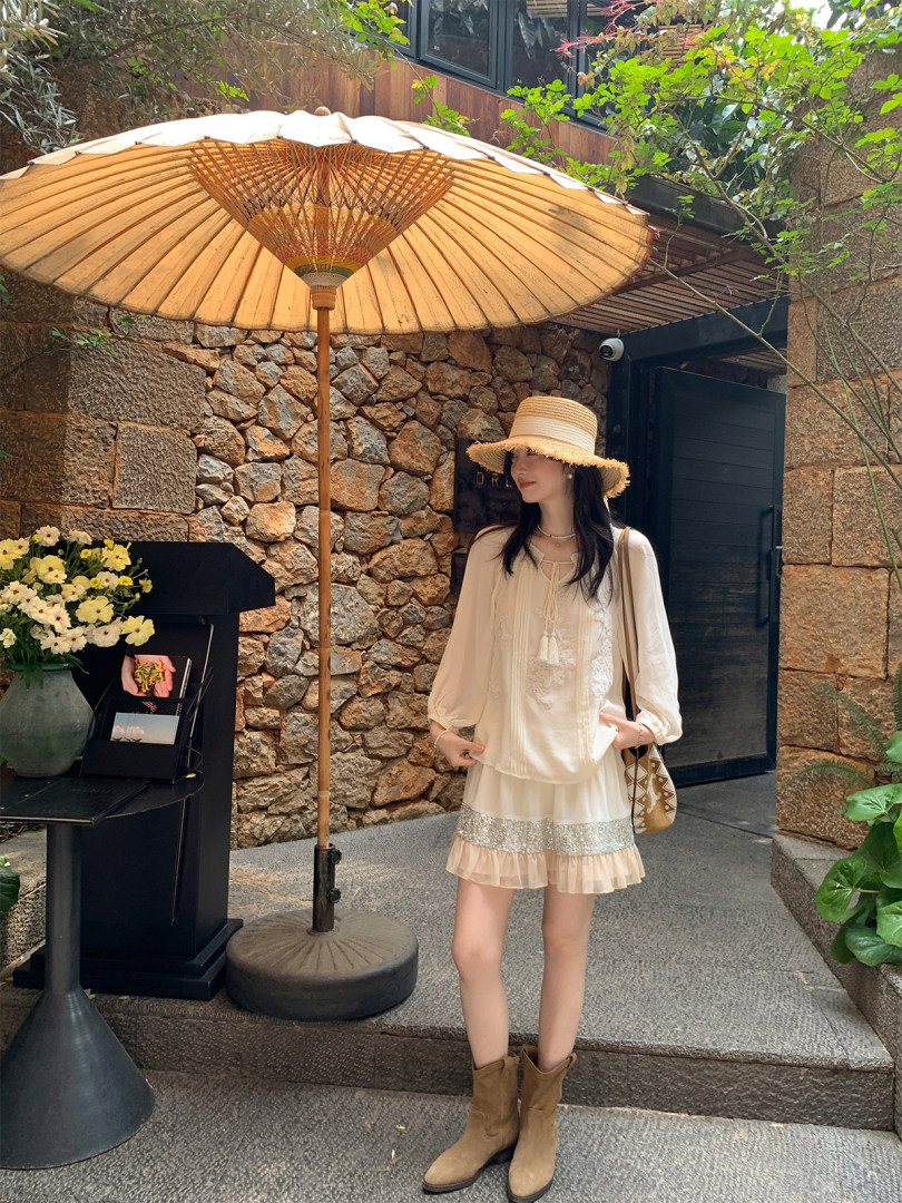 Woman wearing a cream boho blouse and skirt with hat and ankle boots outdoors