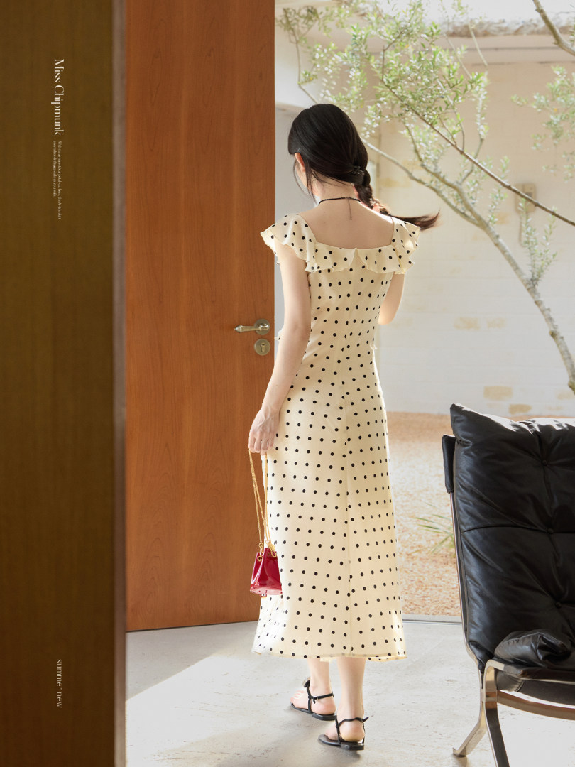 Model wearing a cream polka dot ruffle dress with black sandals.