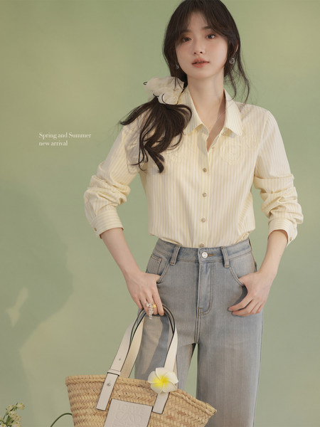Model wearing a cream striped blouse with light blue jeans and a woven straw handbag