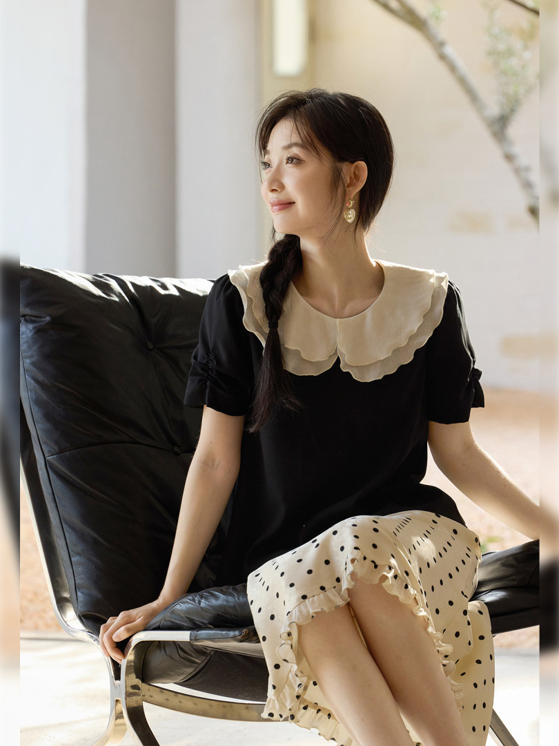 Woman wearing a black dress with a cream scalloped collar and polka dot skirt