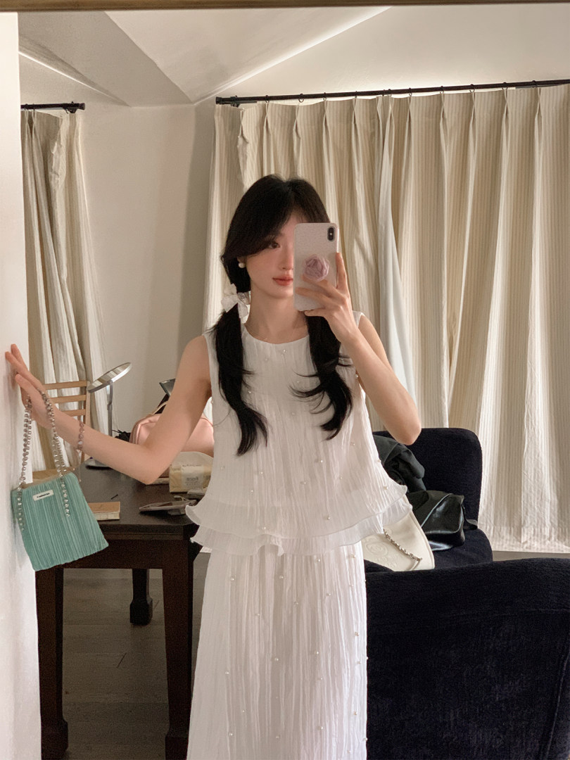 Woman wearing a white sleeveless pleated outfit in a mirror selfie