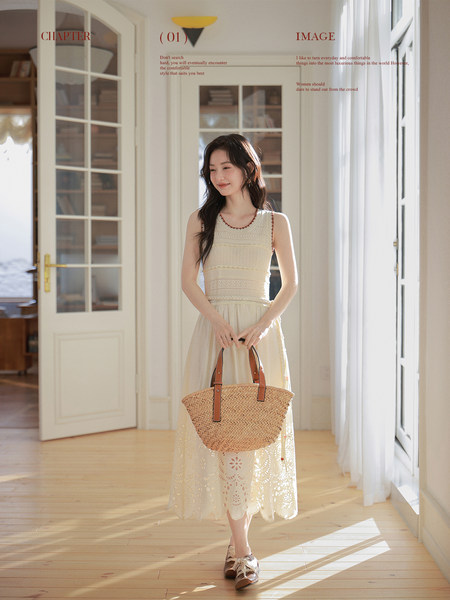 Woman wearing a cream lace sleeveless dress and holding a woven straw tote bag