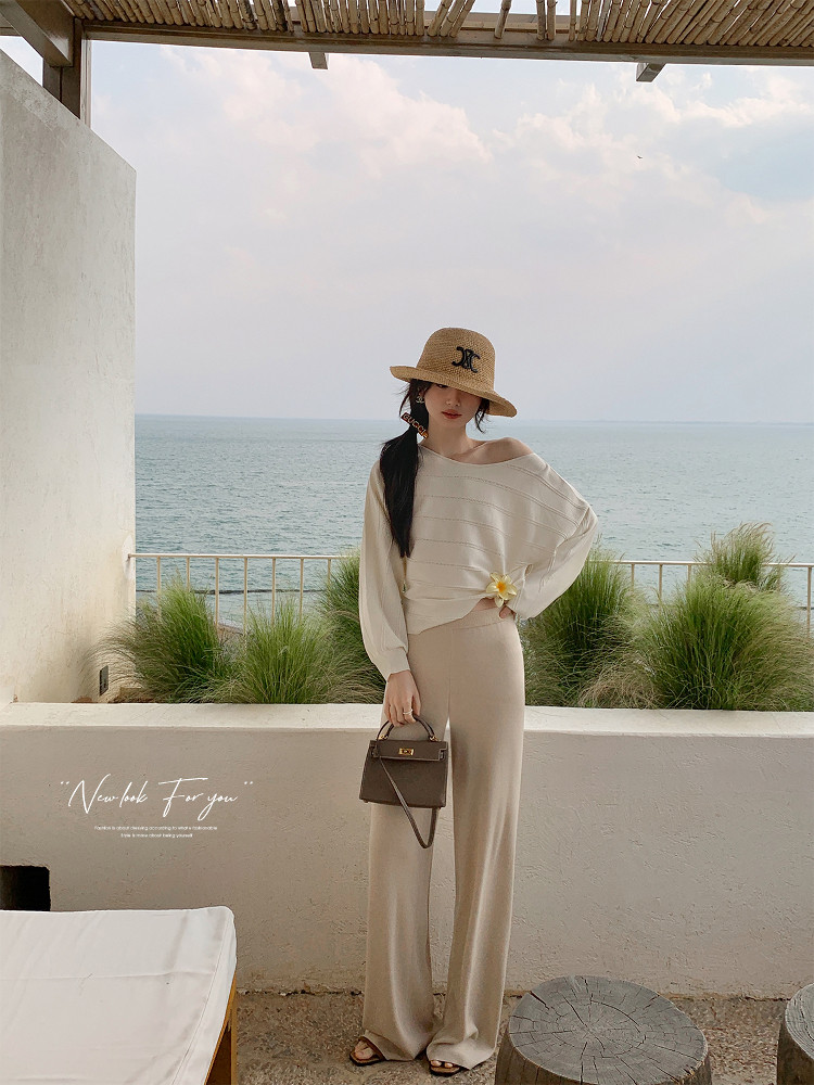Woman modeling a beige beach outfit with hat and handbag by the sea