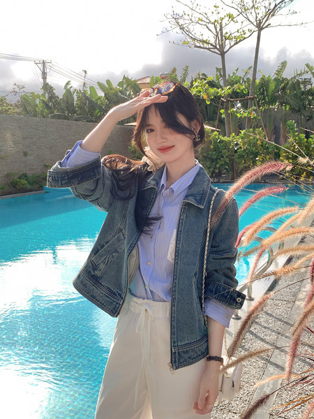 Woman wearing a denim jacket with a light shirt and white pants by a pool