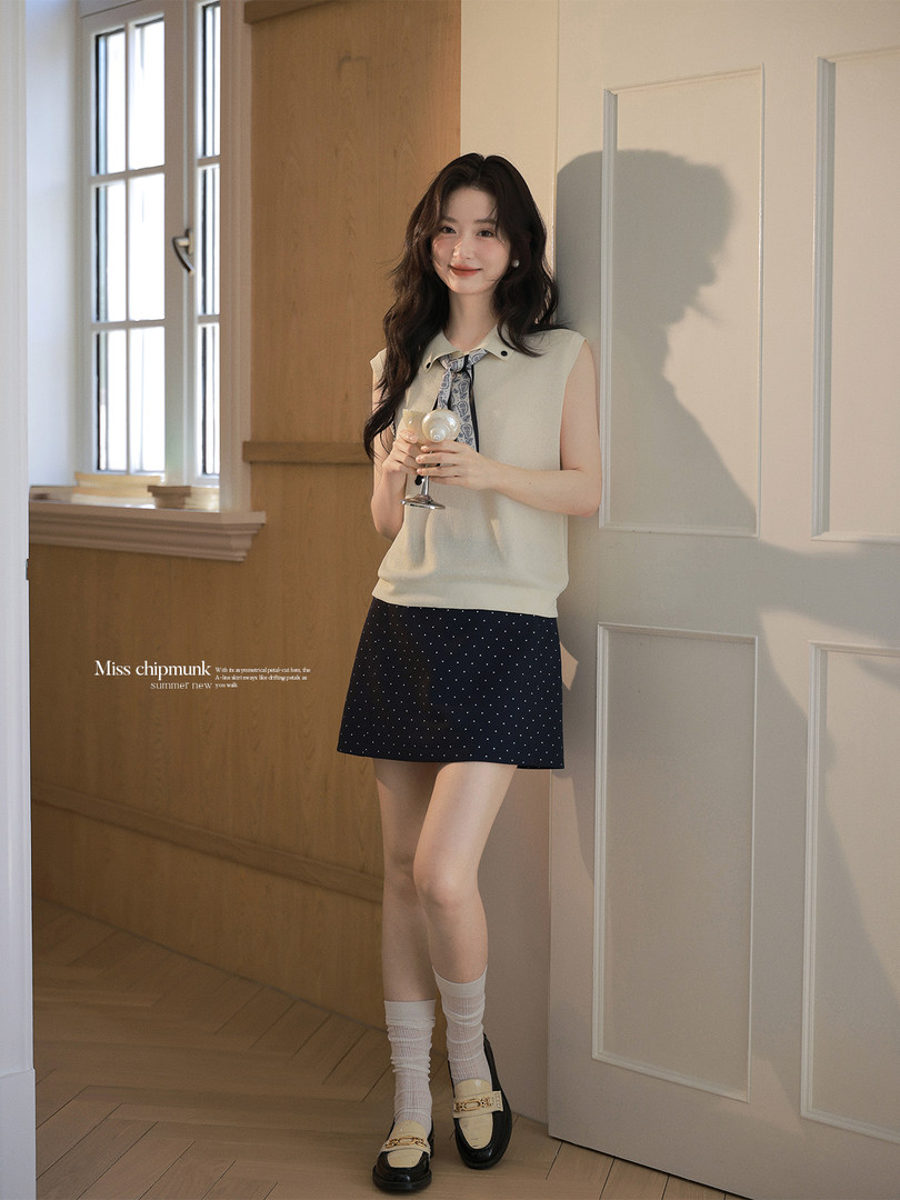 Model wearing a sleeveless cream top and navy polka dot mini skirt outfit