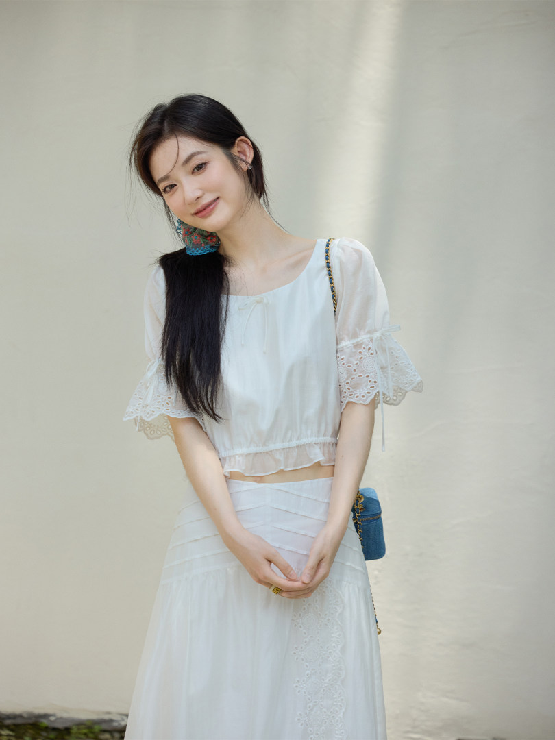Woman wearing a white airy two-piece outfit with lace-trimmed sleeves and skirt