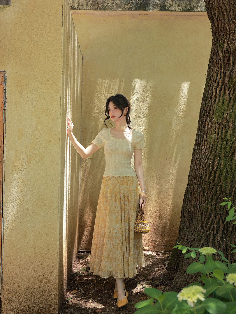 Woman modeling a light yellow knit top with a flowing patterned skirt outdoors