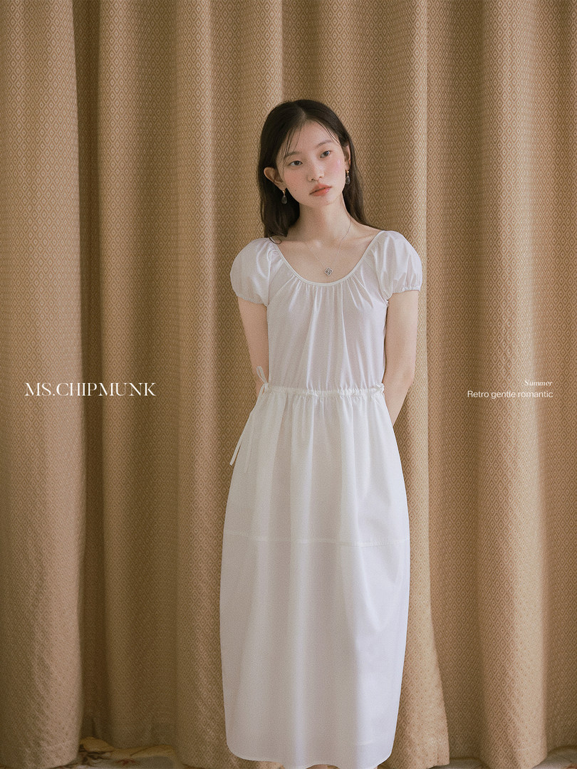 Woman wearing a white puff-sleeve dress against a patterned curtain backdrop