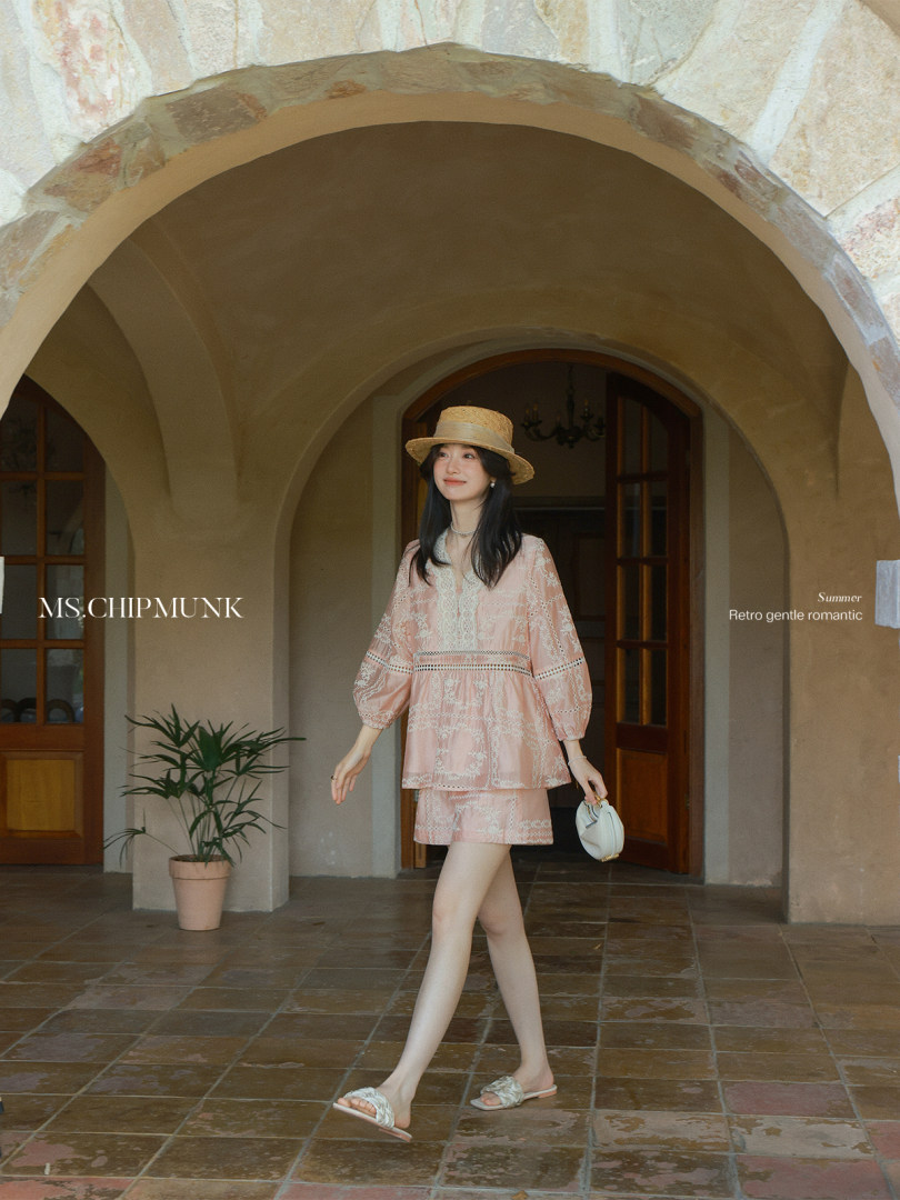 Model wearing a pink lace summer outfit with a straw hat and small handbag