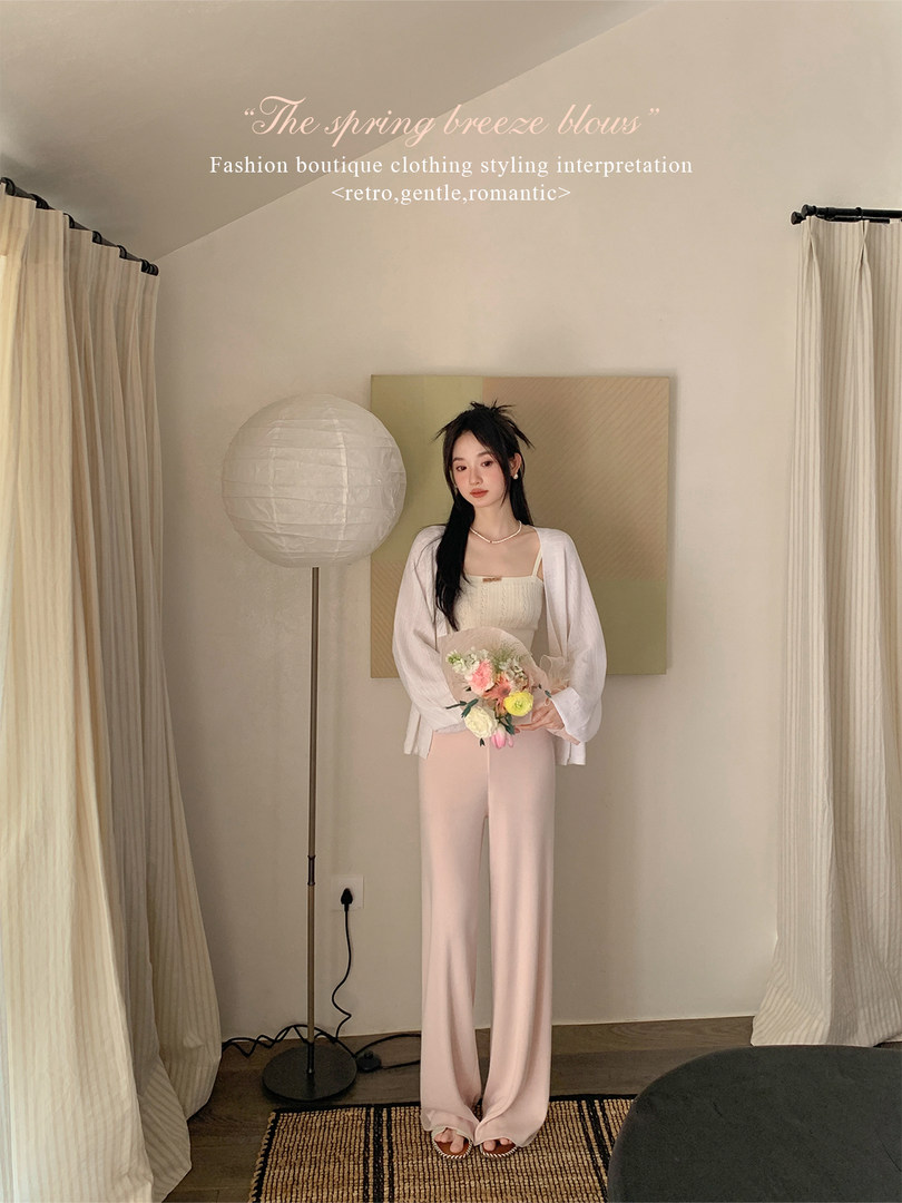 Model wearing a light pastel blouse and pink wide-leg pants in a soft fashion pose