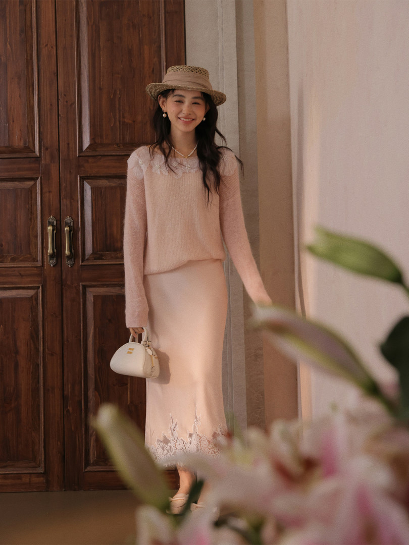 Woman wearing a light pink knit sweater and skirt set with a straw hat and small handbag