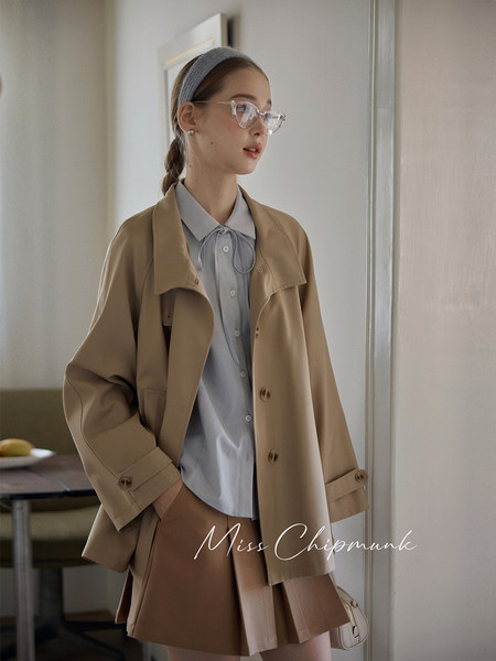 Woman wearing a beige trench coat over a light blue blouse and pleated skirt