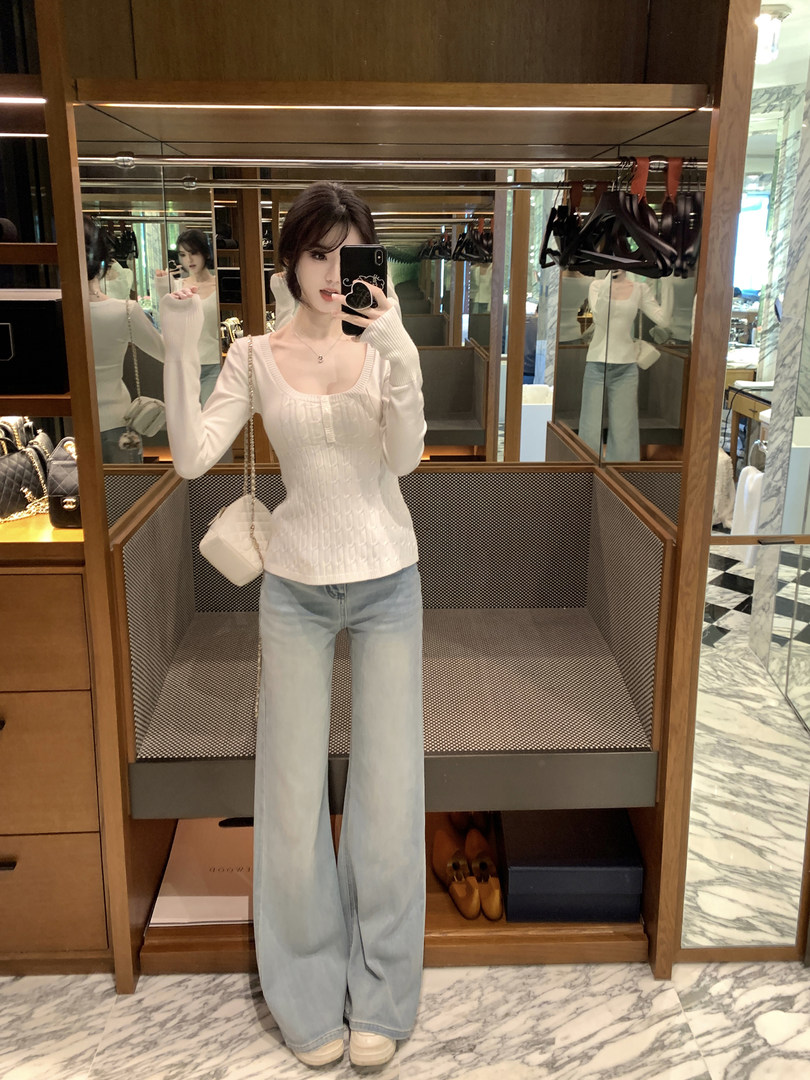 Woman wearing white ribbed long-sleeve top and light blue wide-leg jeans, taking mirror selfie in store fitting room