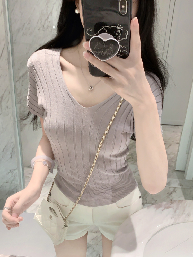 Woman taking mirror selfie wearing ribbed V-neck top and white shorts with a chain strap bag.