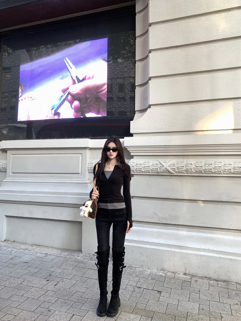 Woman wearing black outfit with boots and holding a bag, standing outdoors
