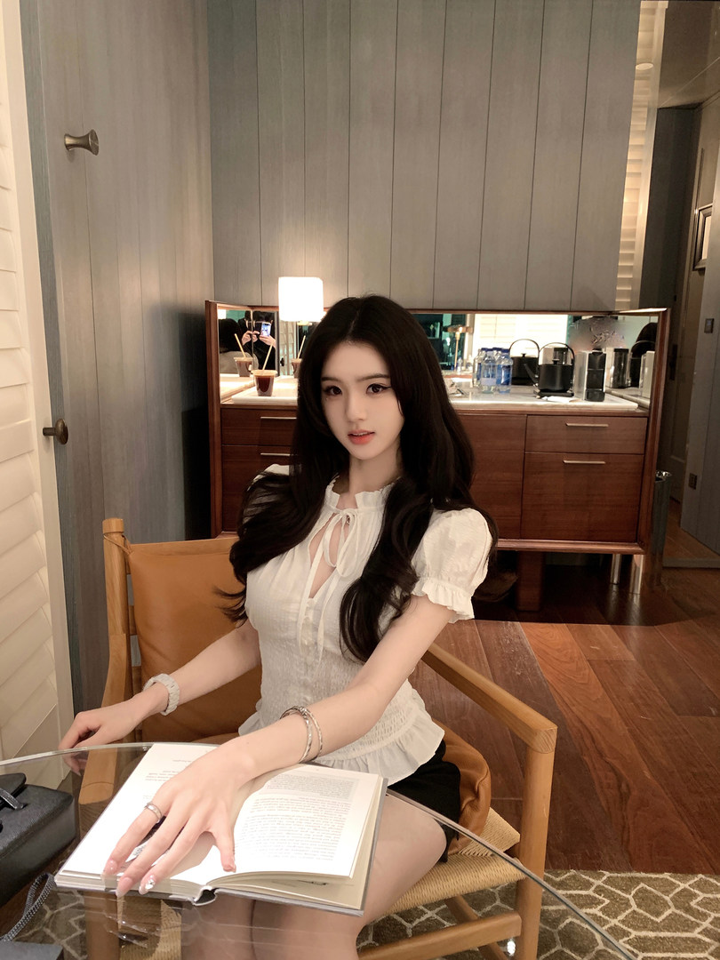 Woman wearing a white blouse with puff sleeves and front tie, seated with an open book