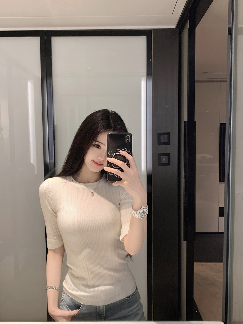 Woman taking mirror selfie wearing a beige ribbed short-sleeve top and jeans