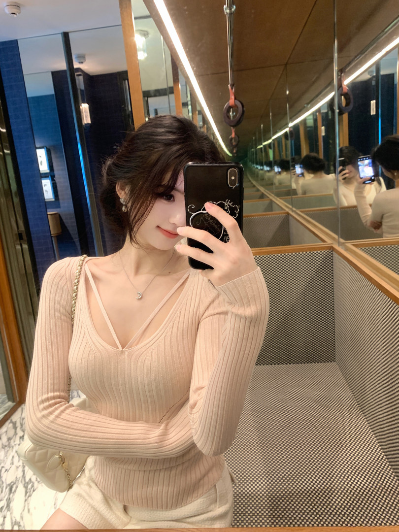 Woman taking mirror selfie wearing beige ribbed long-sleeve top with deep V-neck