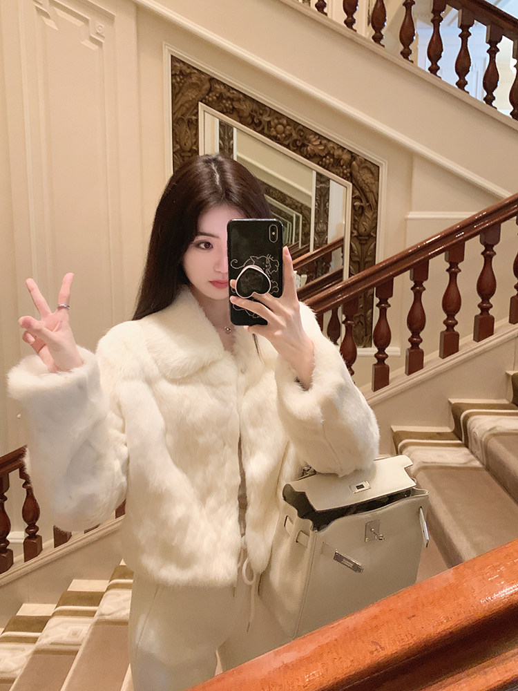 Woman taking a mirror selfie wearing a white faux fur coat and holding a handbag.