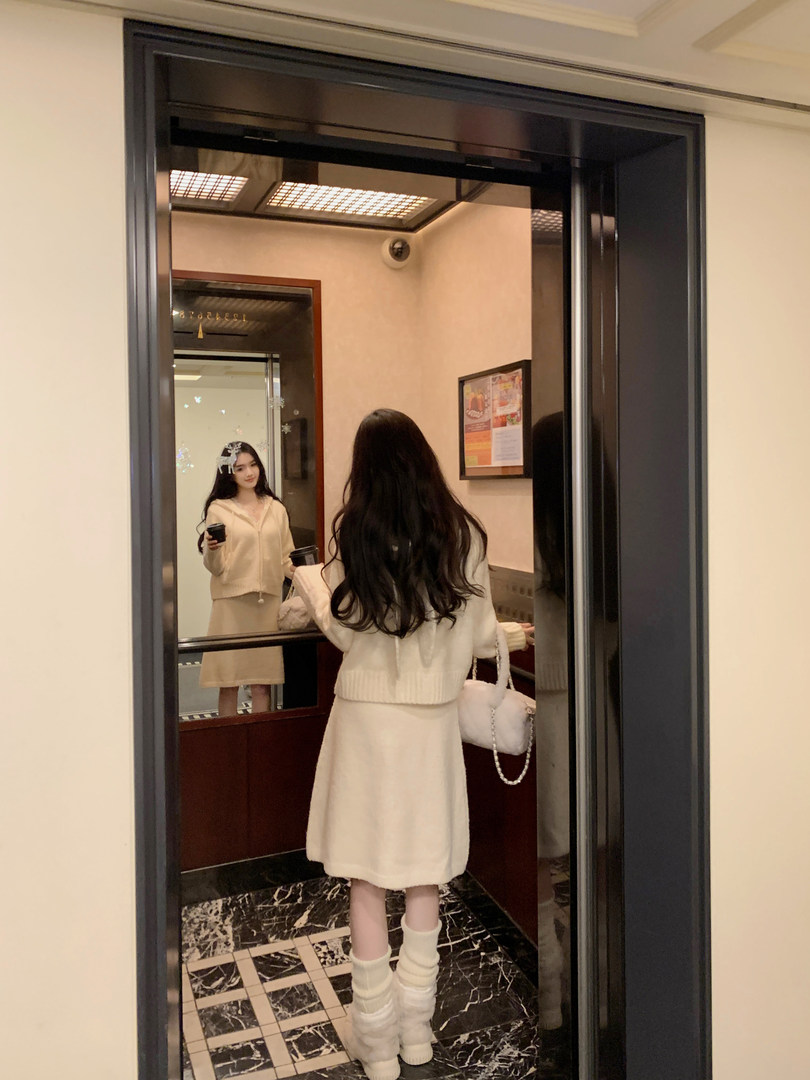 Woman wearing a cream-colored knit set with matching boots, standing in front of a mirror.