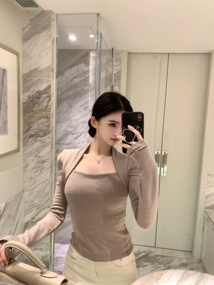 Woman taking mirror selfie wearing a beige long-sleeve top and light-colored pants