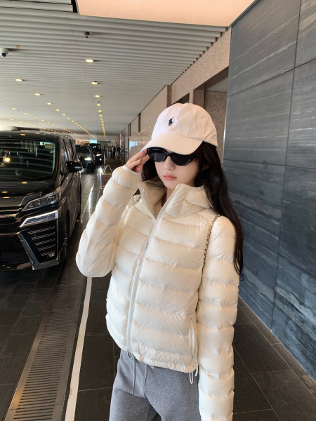Woman wearing white puffer jacket, white cap, and sunglasses in a covered driveway