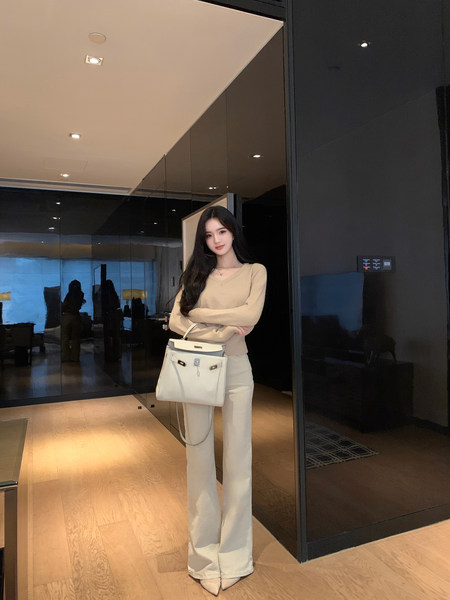 Woman wearing beige sweater and white wide-leg pants, holding white handbag