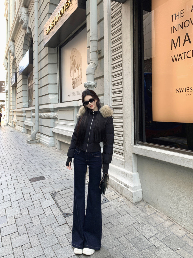 Woman wearing a black puffer jacket with fur collar, dark jeans, and white sneakers on a city street.