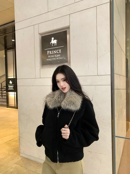 Woman wearing a black coat with a fur collar standing in front of a hotel sign