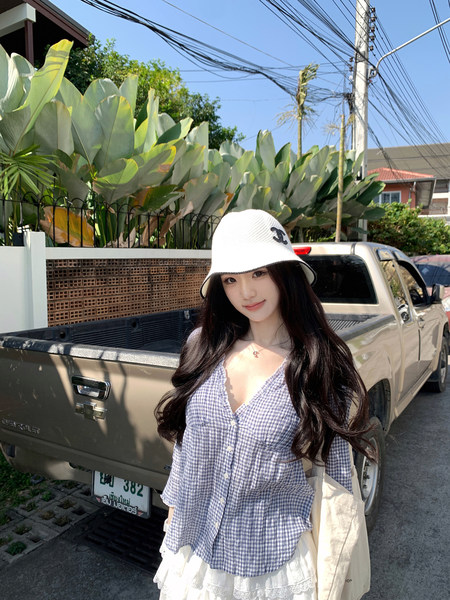 Woman wearing a white bucket hat and blue checkered shirt standing in front of a pickup truck.