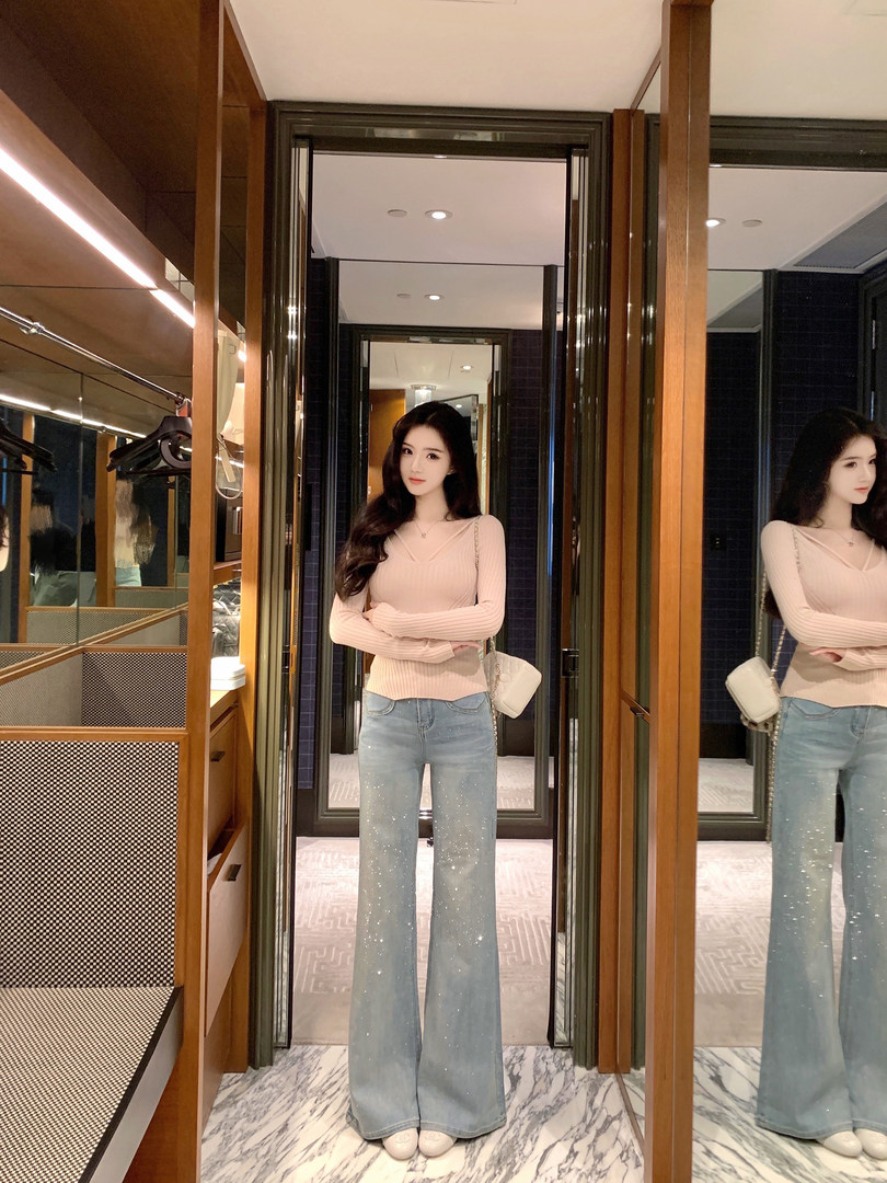 Woman wearing a pink ribbed long-sleeve top and light blue sparkly flare jeans, standing in front of mirrors.