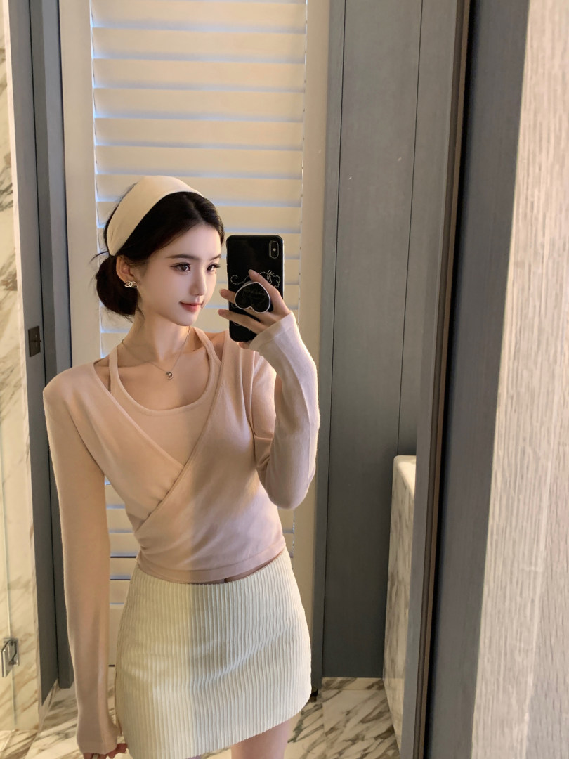 Woman taking mirror selfie wearing beige long-sleeve wrap top and ribbed mini skirt