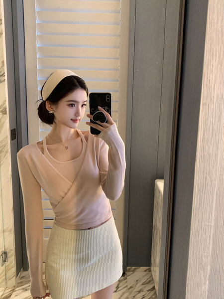 Woman taking mirror selfie wearing beige long-sleeve wrap top and ribbed mini skirt