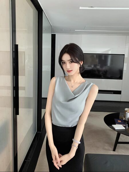 Woman wearing a light gray sleeveless top with draped neckline and black pants in a modern interior