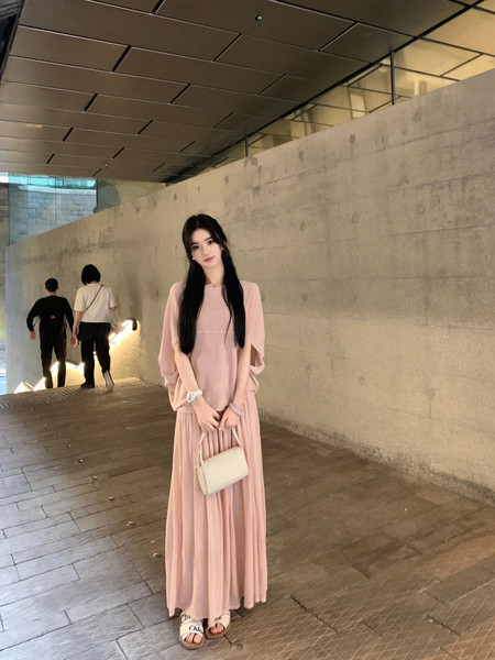 Woman wearing a pink dress with a white handbag, standing in a modern indoor setting.