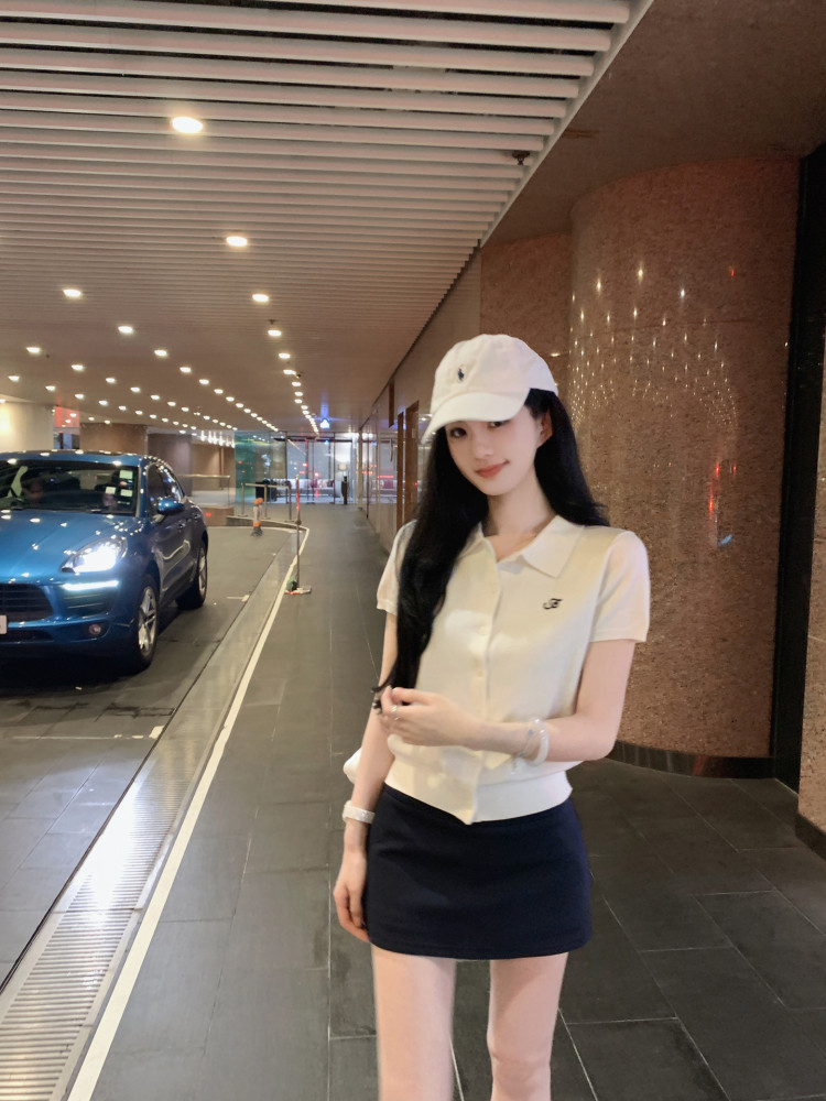 Woman wearing a white polo shirt, black skirt, and white cap in a parking garage.