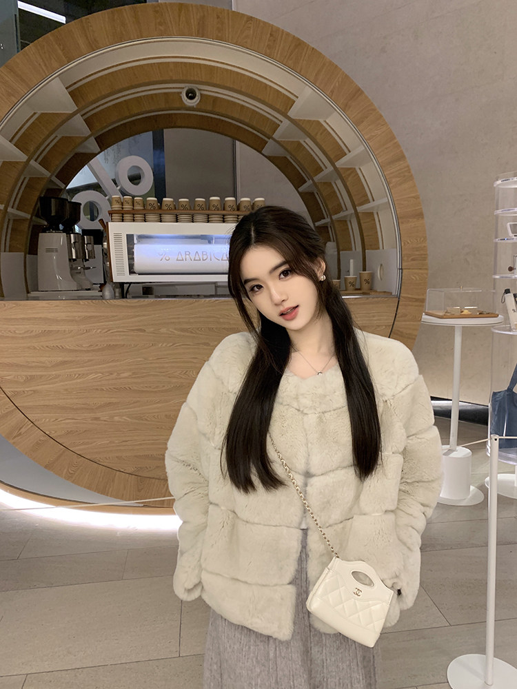 Woman wearing a cream faux fur coat with a white quilted handbag in a modern café setting