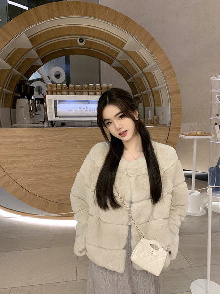 Woman wearing a cream faux fur coat with a white quilted handbag in a modern café setting