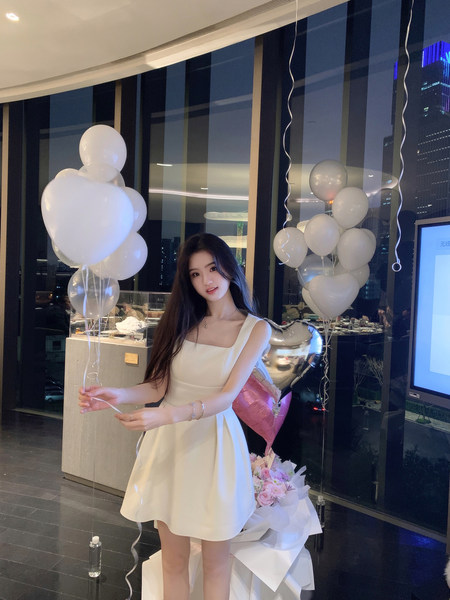 Woman wearing a white dress with balloons and flowers in the background