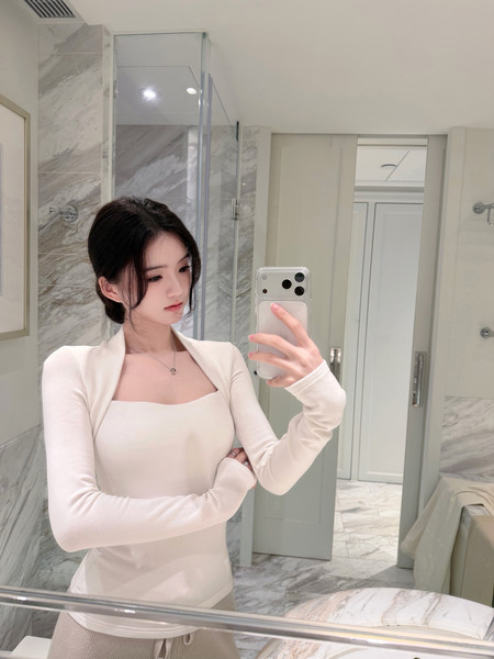 Woman taking mirror selfie wearing a white long-sleeve top with square neckline