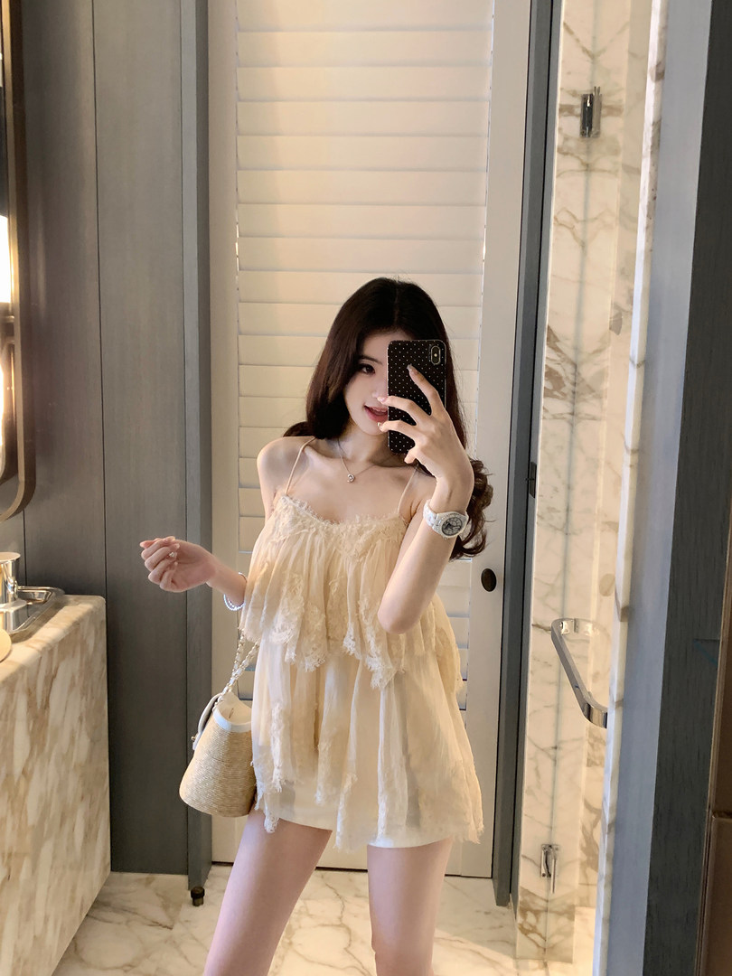 Woman taking mirror selfie wearing a light-colored lace-trimmed camisole dress with a straw bag.