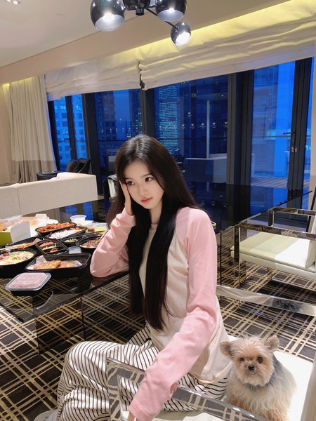 Woman wearing pink long-sleeve top and striped pants sitting with a dog in a hotel room