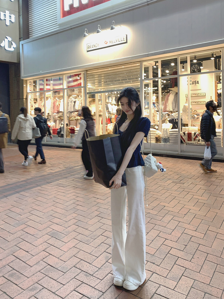 Woman wearing a navy blue top and white wide-leg pants standing outside a store.