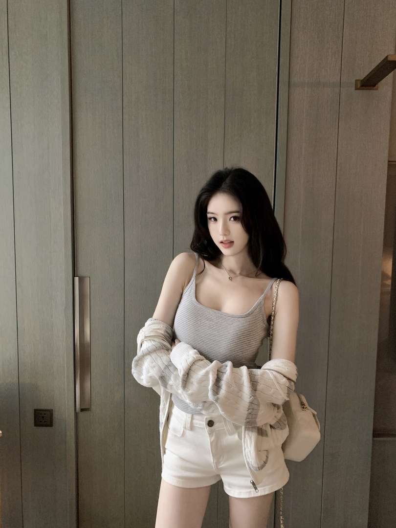 Woman wearing striped tank top, white shorts, and a knit cardigan with a beige bag.