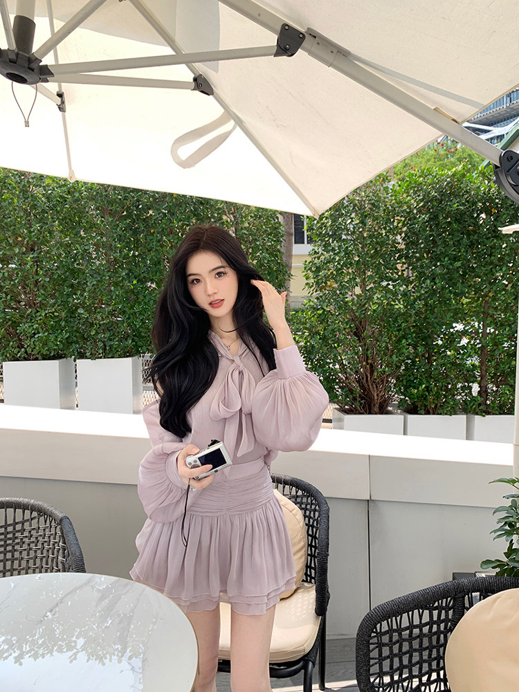 Woman wearing a light purple dress with puffed sleeves and a bow neckline, standing under an umbrella.